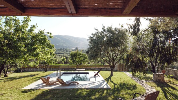 Un espace piscine comprenant deux chaises longues et une table, le tout entouré d’un mur de pierre et d’une végétation luxuriante.
