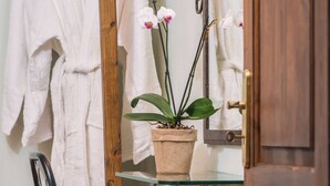 Une salle de bain avec un meuble-lavabo en bois, un miroir, un peignoir blanc, une orchidée en pot et un coussin rayé sur une chaise.