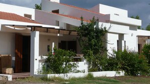 A modern white building with a red-tiled roof, a covered porch, and a garden area with plants and flowers. - Villa nestled in the countryside with spectacular views for 6 people (Carloforte)