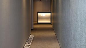 A narrow hallway with a carpeted floor, a reception desk at the end, and walls with a textured finish. - GRAND BASE Hakata (Fukuoka)