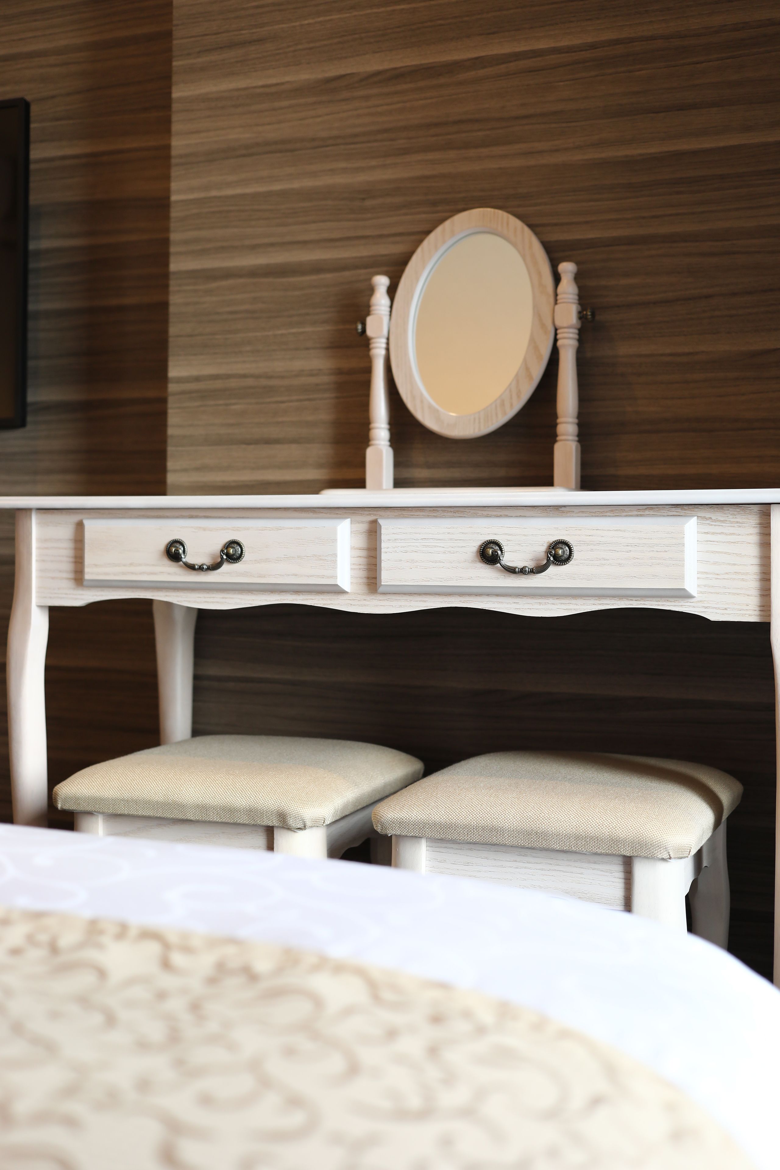 A white vanity with a mirror and two drawers, a bench, and a patterned bedspread.