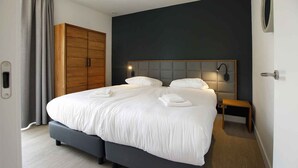 A modern bedroom with a large bed, grey upholstered headboard, bedside lamps, and a wooden wardrobe. - Eagle 8p - Four Bedroom Villa, Sleeps 8 (Oosterhout)