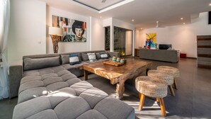 A modern living room with a sectional sofa, a wooden coffee table, and wicker ottomans. - Private Pool Villa | Daily Housekeeping | Seminyak (Seminyak)