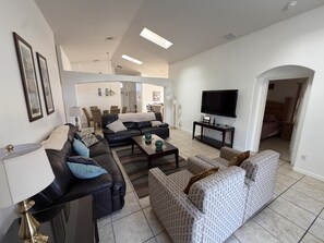 A living room with a sofa, armchair, coffee table, TV, and dining area.