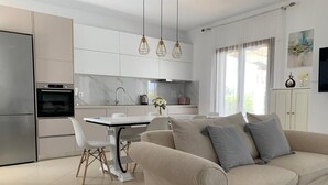 Une cuisine moderne avec des meubles blancs, une table à manger avec des chaises et un canapé beige agrémenté de coussins.