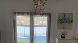 Un coin repas avec une table blanche, un vase de fleurs et une vue sur la mer, visible à travers de grandes fenêtres.