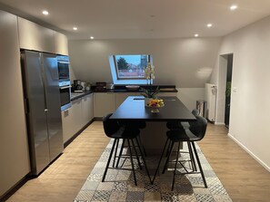 Una cocina moderna con una isla grande, electrodomésticos de acero inoxidable y vistas de la ciudad a través de un ventanal.