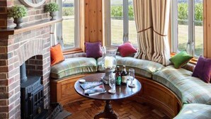 A cozy room with a fireplace, a round table, and a curved bench with cushions. - 4 bedroom stunning rural position near Jurassic coast ! (Dorchester)