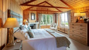 A cozy wooden cabin bedroom with a large bed, a dresser, a chair, and a window with curtains. - 4 bedroom stunning rural position near Jurassic coast ! (Dorchester)