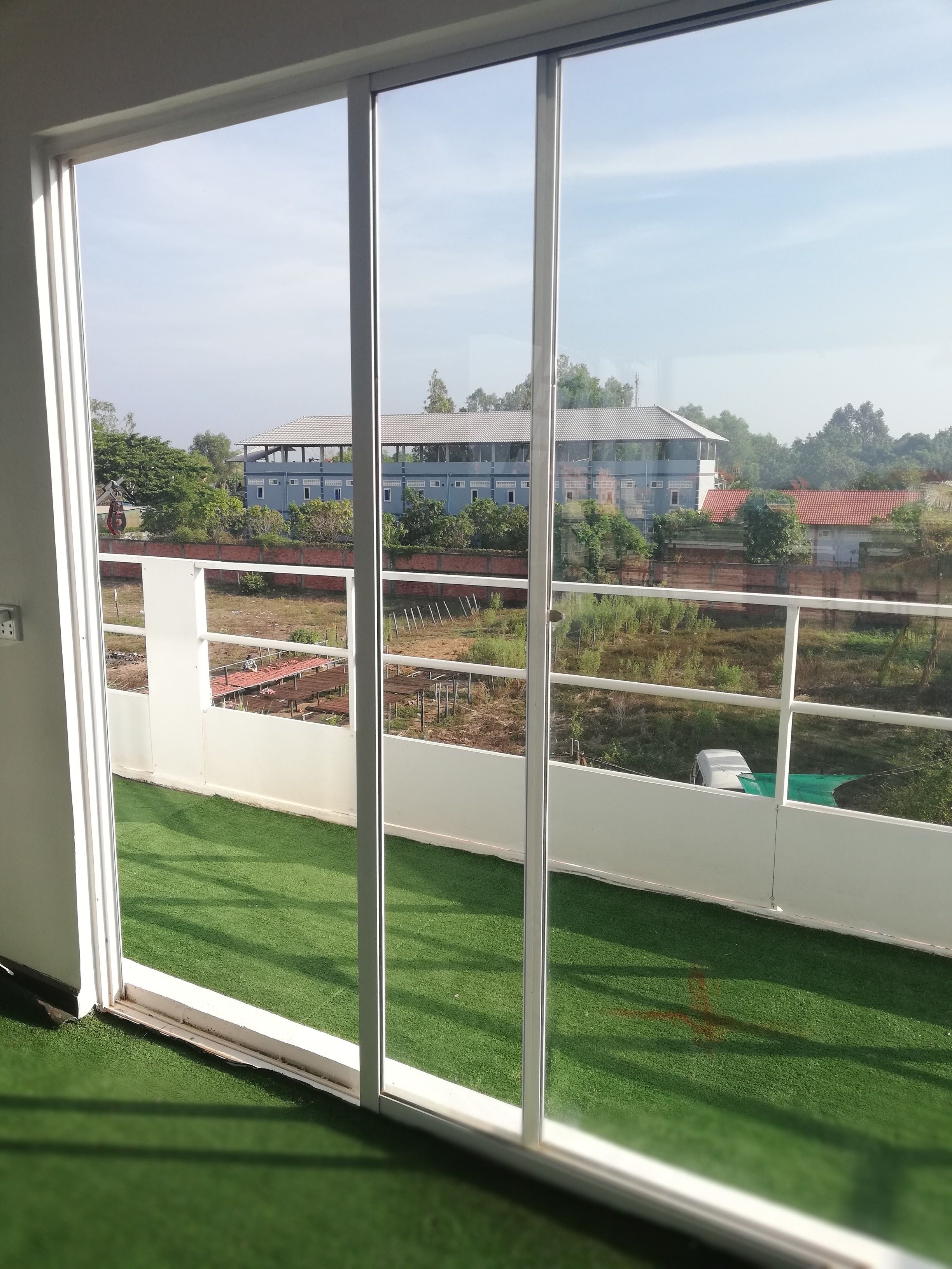 A room with a large window overlooking a grassy area and a building with a red roof.