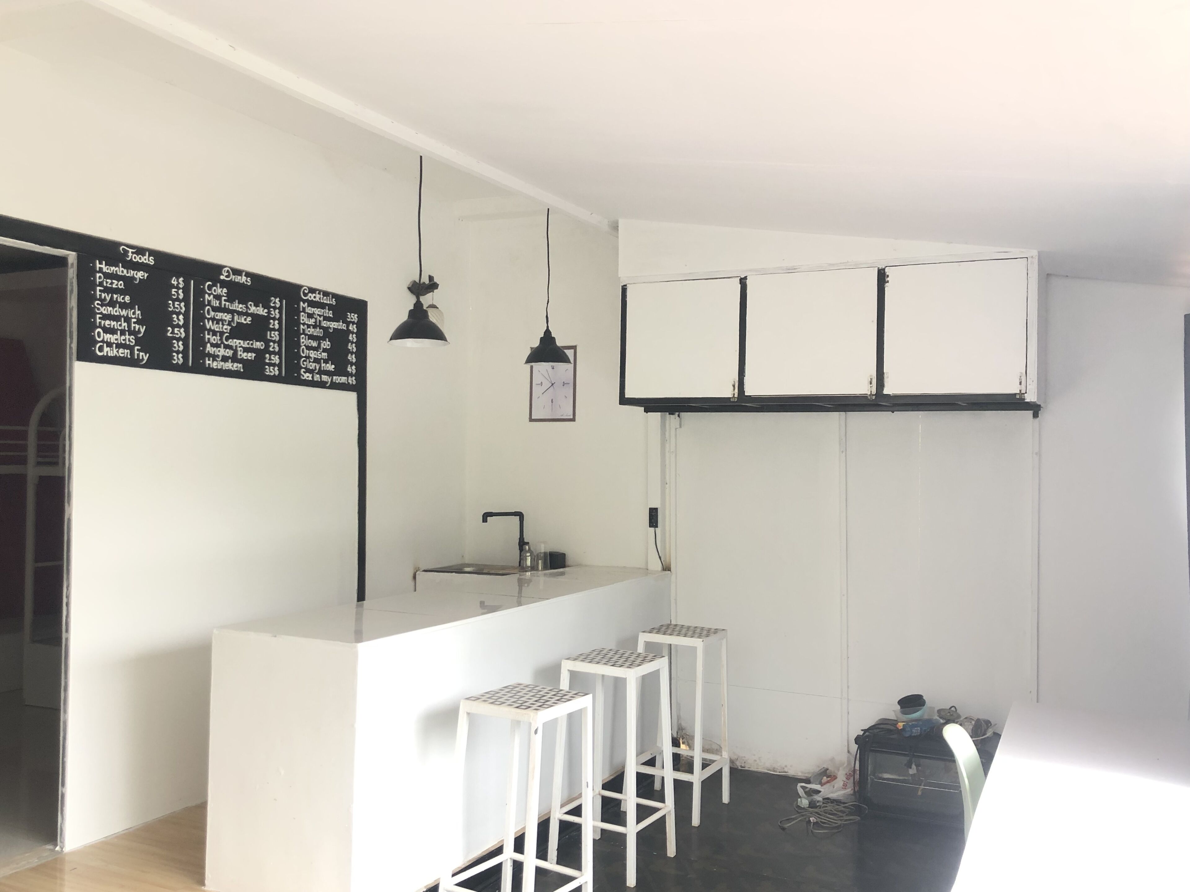 Una cocina compacta con encimera blanca, taburetes de bar, lámpara colgante y un reloj de pared.