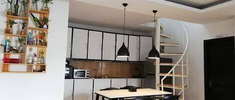 A modern kitchen with white cabinets, a microwave, and a dining area with a table and chairs. There is a spiral staircase leading to an upper level.