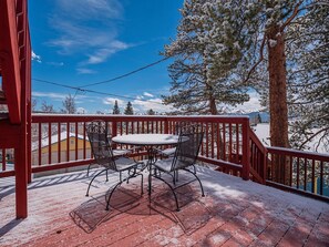 A snow-covered deck with a table and chairs, overlooking a snowy landscape and trees. - The Governor's Mansion — 6BR Sleeps 14, 3 Private Units, Hot Tub, Sauna (Leadville)