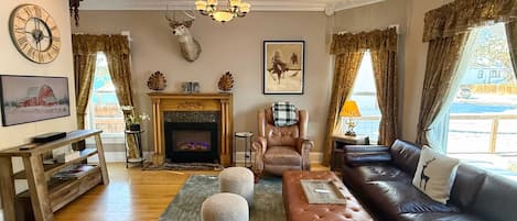 Un salon chaleureux avec une cheminée, des meubles en cuir, une tête de cerf accrochée au mur et une grande horloge.