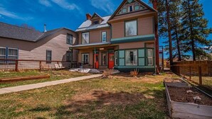 Une maison à deux étages avec un porche à l’avant, une porte rouge et une grande fenêtre donnant sur la cour.