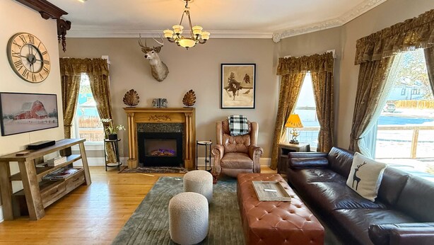 Un salon chaleureux avec une cheminée, des meubles en cuir, une tête de cerf accrochée au mur et une grande horloge.