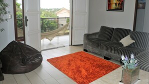 A living room with a sofa, a bean bag, a rug, and a view of the outdoors through an open door.