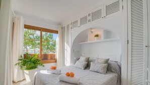 Quarto com cama grande, planta em vaso e janela com vista para árvores.