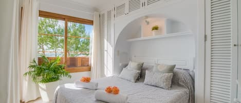 A bedroom with a large bed, a potted plant, and a window with a view of trees.