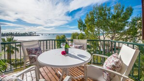 Uma varanda com uma mesa e cadeiras brancas, com vista para uma praia e o mar.