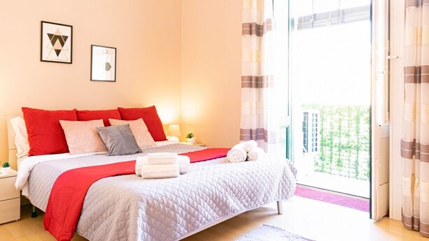 Ein Schlafzimmer mit Bett, Kissen, einem Nachttisch und einem Fenster mit Vorhängen.