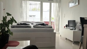 Een slaapkamer met een bed, een bureau, een stoel, een potplant en een raam met gordijnen.