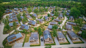 Une vue aérienne d’un quartier résidentiel composé de plusieurs maisons dotées de panneaux solaires, entouré de verdure et offrant une vue lointaine sur des éoliennes.