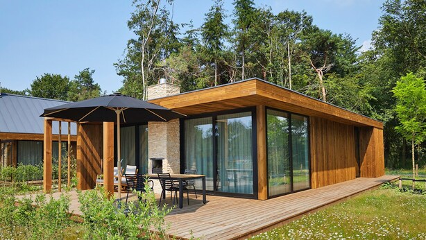 Une cabane moderne en bois, dotée d’une terrasse, de murs en verre et d’un espace extérieur aménagé et couvert.