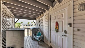 A covered porch with a wooden floor, a wheelchair, and a door with a number plate.