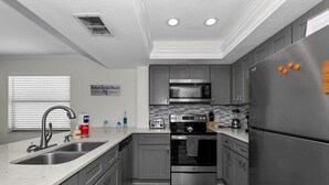 A modern kitchen with grey cabinets, stainless steel appliances, a double sink, and a sign indicating the location.