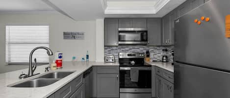 A modern kitchen with grey cabinets, stainless steel appliances, a double sink, and a sign indicating the location.