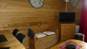L’intérieur d’un chalet en bois, avec un lit en bois, un téléviseur posé sur un meuble, une table à manger et une horloge murale.