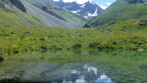 Un lac de montagne aux eaux cristallines, entouré de collines verdoyantes et de montagnes rocheuses.