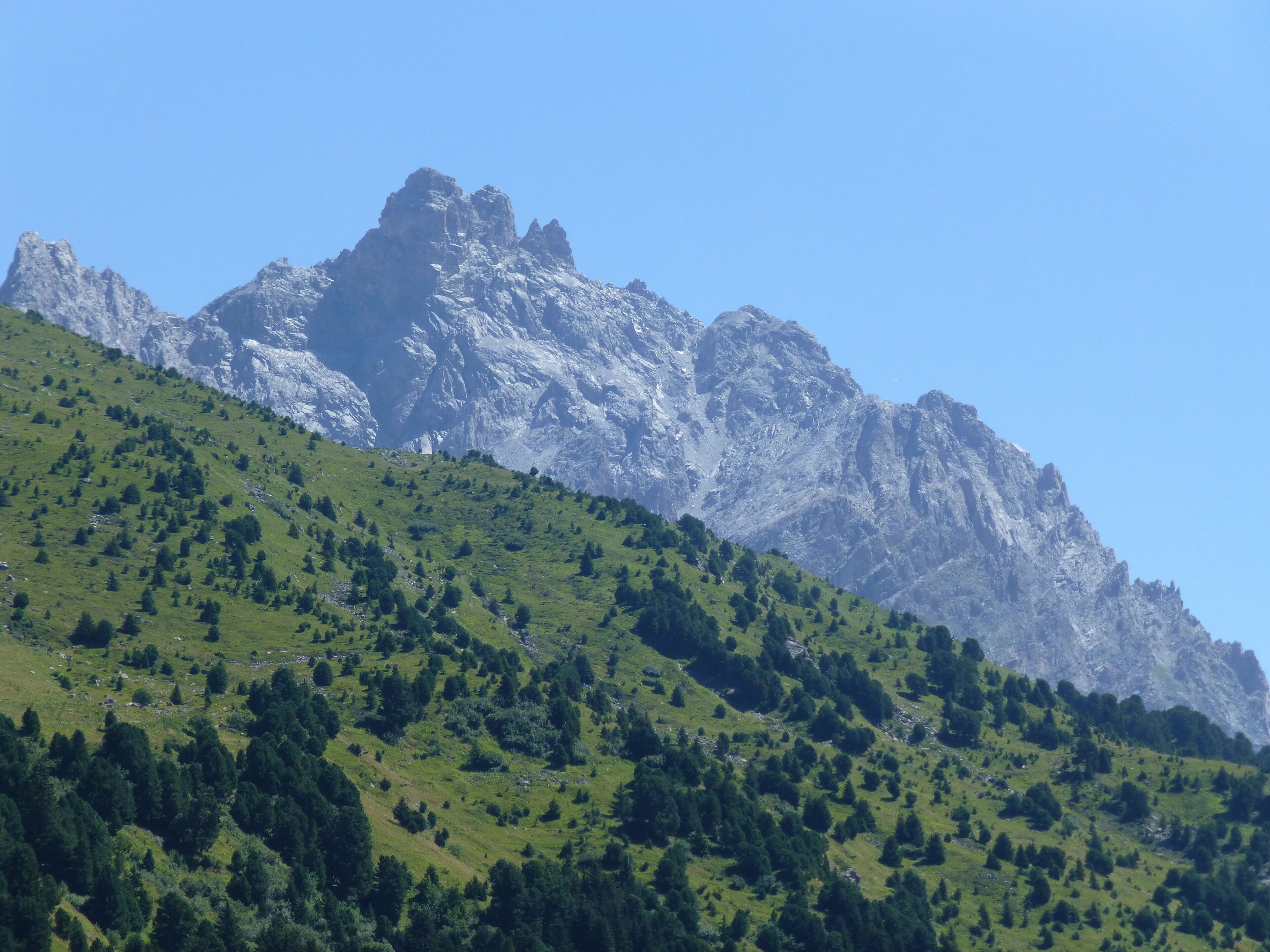 A mountainous landscape with a prominent rocky peak and a green hillside.
