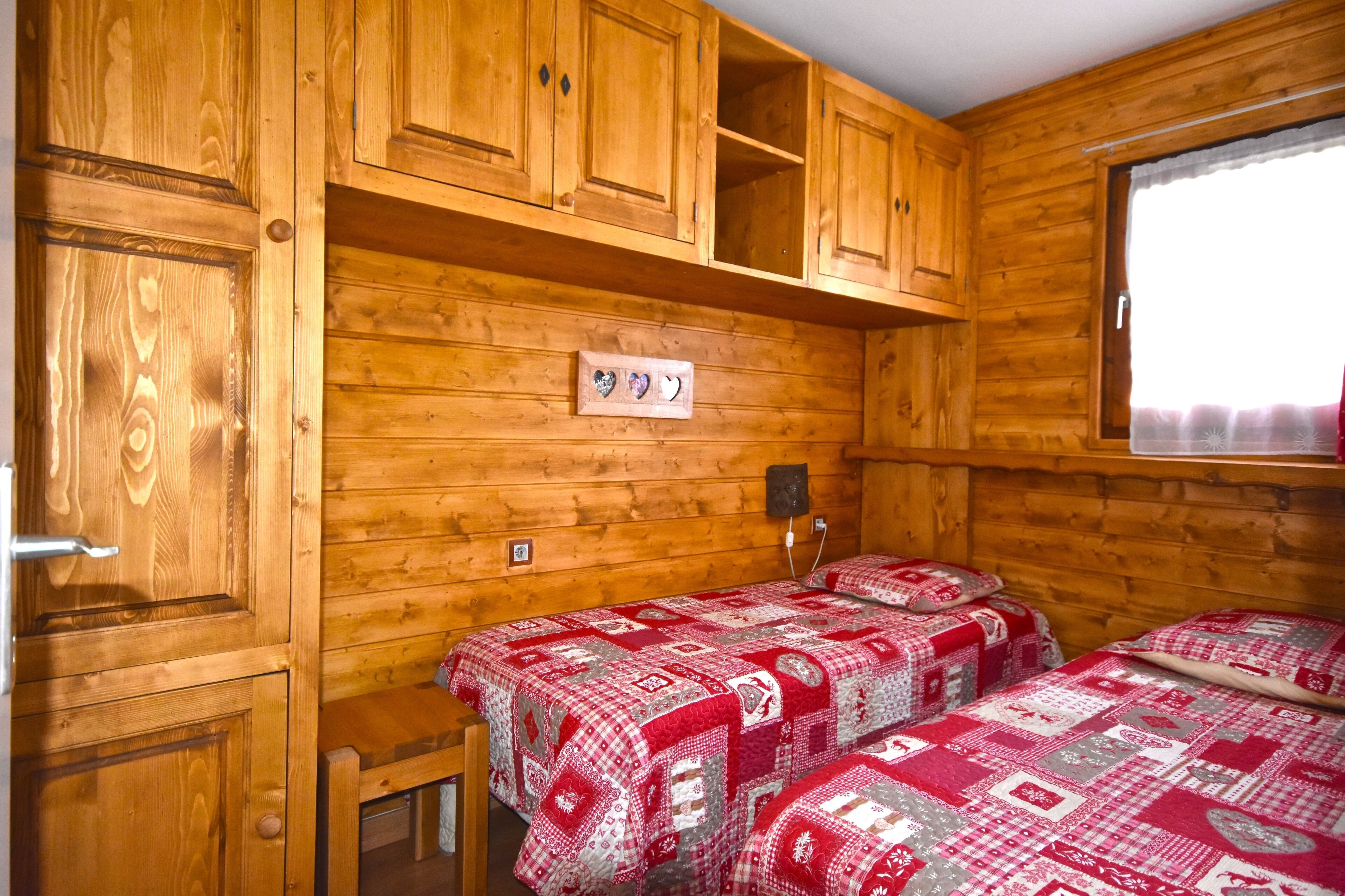 Una baita con pareti in legno, due letti con biancheria rossa e bianca, una finestra con tende e una porta in legno.