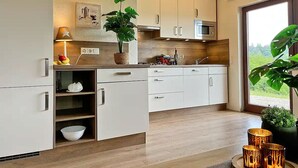A modern kitchen with white cabinets, a microwave, and a large window. - Vulkaneifel Type L-A4 (Gerolstein)