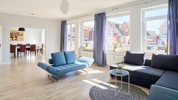 Una sala de estar moderna con un sofá azul, un sofá oscuro y un comedor con mesa y sillas.