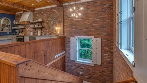 A rustic kitchen with exposed brick walls, wooden beams, and a hanging light fixture. - The Loft on Trade Street | Downtown Tryon | Near TIEC (Tryon)