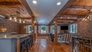 A spacious kitchen with a large island, wooden beams, and hanging pendant lights. - The Loft on Trade Street | Downtown Tryon | Near TIEC (Tryon)