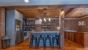 A kitchen with a central island, bar stools, and a brick wall. - The Loft on Trade Street | Downtown Tryon | Near TIEC (Tryon)