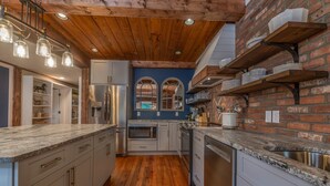 A kitchen with wooden floors, white cabinets, a brick accent wall, and built-in shelves. - The Loft on Trade Street | Downtown Tryon | Near TIEC (Tryon)