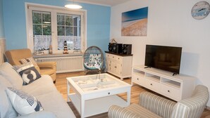 Una sala de estar con sofá, sillón, mesa de centro, mueble para televisión y objetos decorativos.