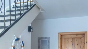 Una escalera con barandilla, una puerta de madera, y una pared con un adorno de aro salvavidas y un cuadro enmarcado.