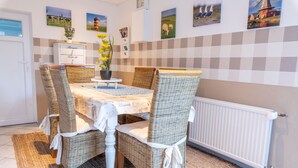 Un comedor con pared a cuadros, sillas de mimbre, una mesa blanca y un radiador.