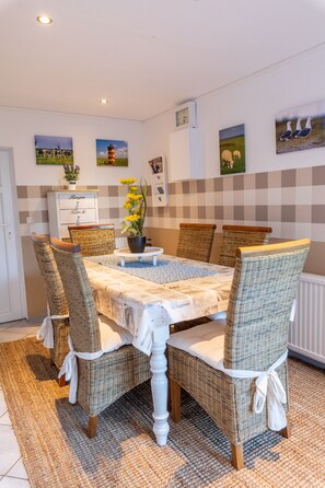A dining area with a round table, wicker chairs, a white cabinet, and wall art.