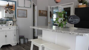 A kitchen with a marble countertop, white bar stools, a welcome sign, and a 'Farm Sweet Farm' sign on the wall. - Unique Farm Cottage, Close to City Feels like Country, One of a Kind! (Colorado Springs)