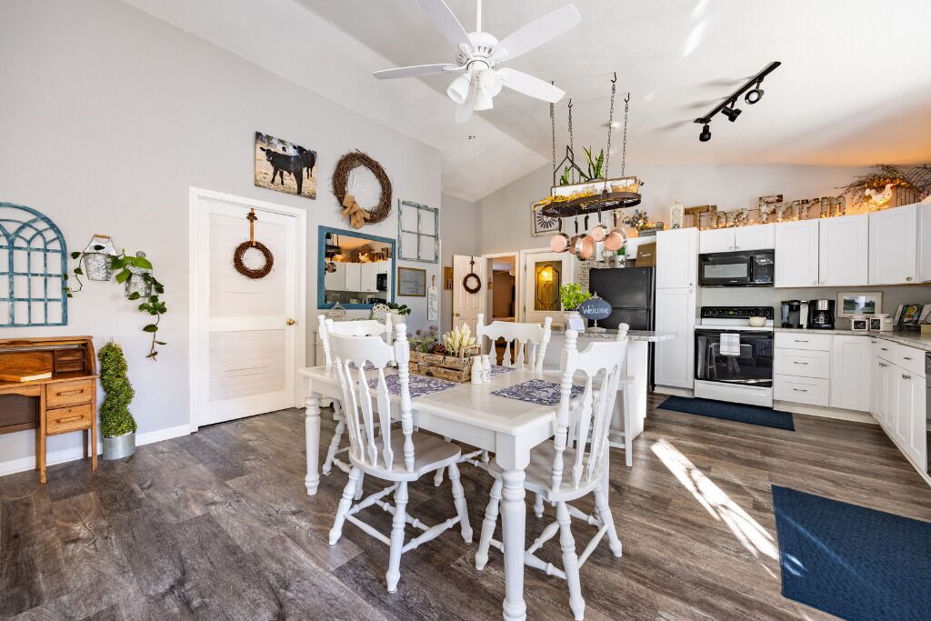A spacious kitchen with white cabinetry, a dining area with a white table and chairs, and a ceiling fan.