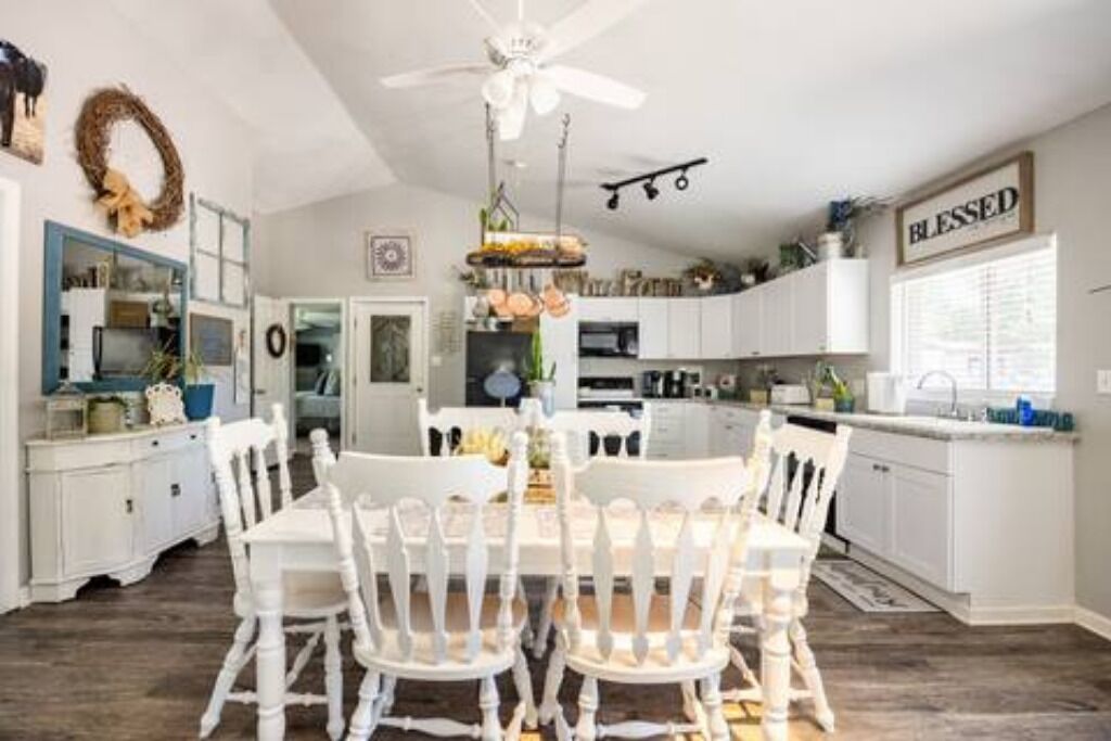 A dining area with a white table and chairs, a chandelier, and a ceiling fan.
