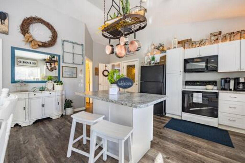 Una cucina moderna con mobili bianchi, un piano di lavoro in granito e una rastrelliera pensile per pentole.
