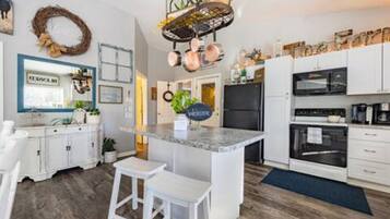 Una cucina moderna con mobili bianchi, un piano di lavoro in granito e una rastrelliera pensile per pentole.